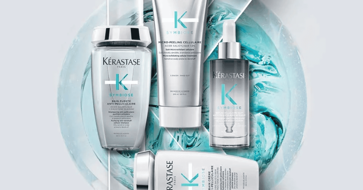 Produtos da linha Kérastase Symbiose dispostos sobre fundo azul translúcido, incluindo shampoo, micropeeling, sérum e tratamento para couro cabeludo e cabelos.