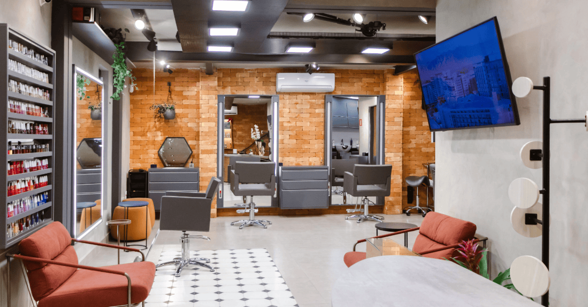 Interior do Beauty.Co.Lab na Vila Nova Conceição, com estações de atendimento, espelhos, poltronas em tons terrosos, parede de tijolos e elementos naturais.